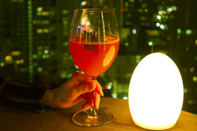 Female's hand holding a glass of cocktail at the rooftop terrace with blurry city aerial night view