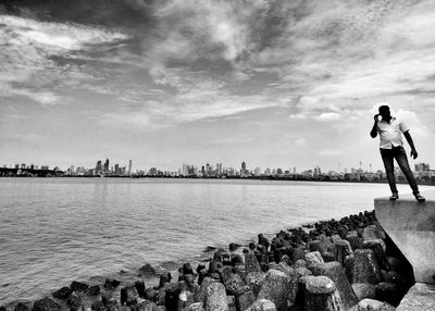Woman standing on retaining wall by cityscape against sky