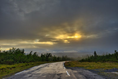 Road by trees against sky during sunset