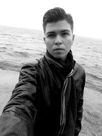 Portrait of young man standing at beach against clear sky