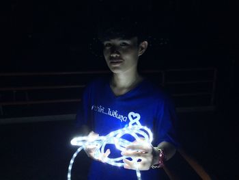 Portrait of young man holding illuminated lighting equipment