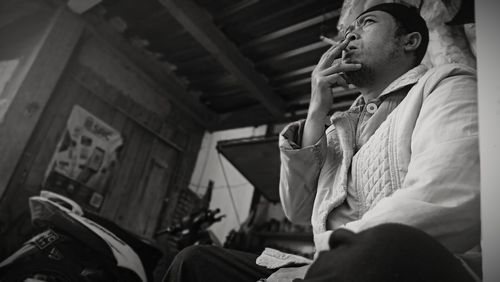 Low angle view of man smoking cigarette while sitting indoors