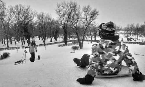 Rear view of people sitting on snow covered field