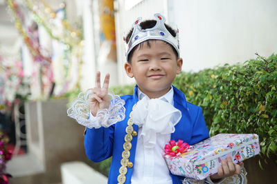 Portrait of smiling boy wearing crown holding gift box while standing in party