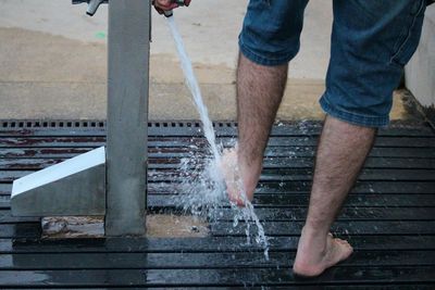 Low section of man washing legs while standing outdoors