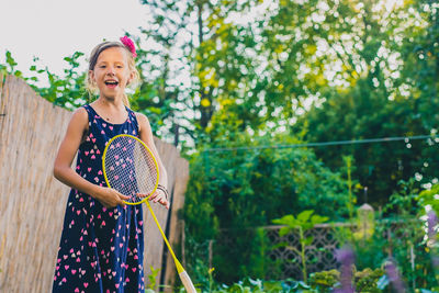 Portrait of girl holding badminton racket while standing against trees