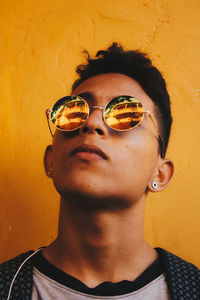 Close-up of young man wearing sunglasses against yellow wall