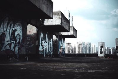 Graffiti on bridge by buildings against sky in city