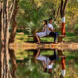 Reflection of young woman sitting on tree by lake