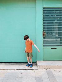 Full length of boy standing on footpath against wall