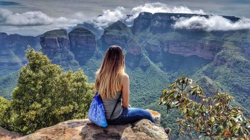 Rear view of woman sitting on rock against mountain