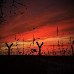 Silhouette fence on field against orange sky