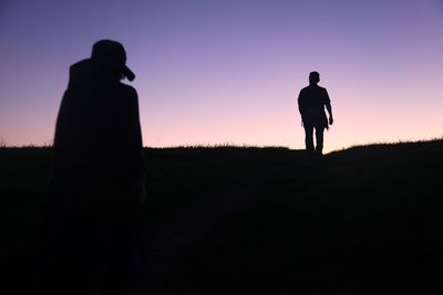 Silhouette of people standing on field at sunset