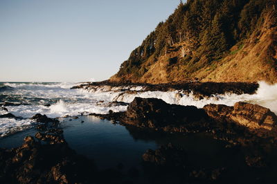 Wave splashing on rocks against clear sky