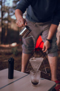 Midsection of man pouring coffee in cup on table