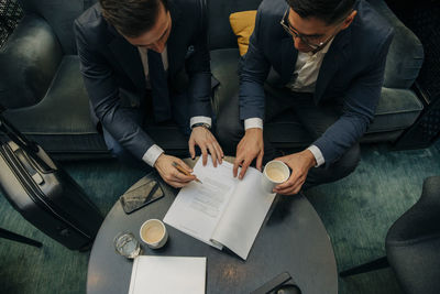 High angle view of young businessman signing contract by male colleague in hotel lounge