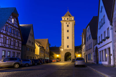 Cars on illuminated street amidst buildings in city against sky at dusk