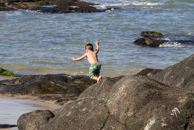 Full length of shirtless boy on rock at beach