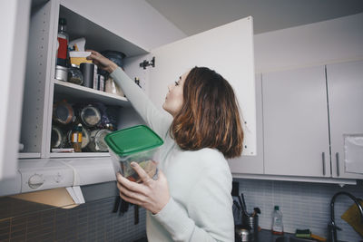 Young woman searching in cabinet at kitchen