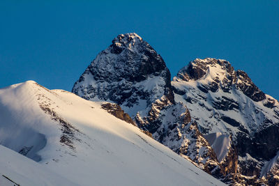 Low angle view of snowcapped mountains against clear blue sky