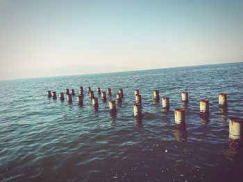 Wooden posts in sea against clear sky