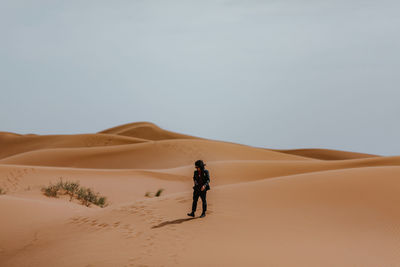Man walking on sand in desert against sky