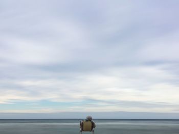 Rear view of person sitting on beach against sky