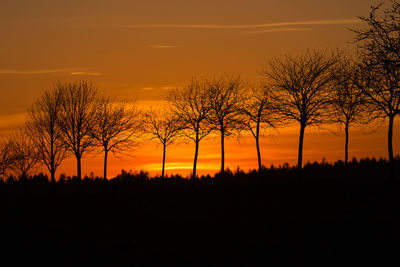 Silhouette trees on landscape against romantic sky at sunset
