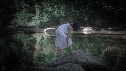 Rear view of woman standing by lake in forest