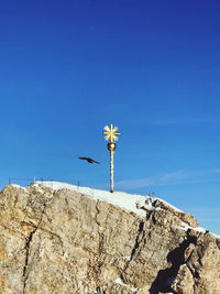 Low angle view of cross on rock against clear blue sky