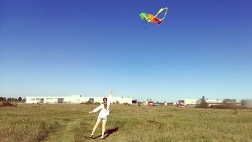 Woman flying kite against clear blue sky