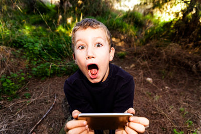 Portrait of boy holding mobile phone while sitting outdoors