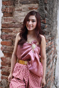 Portrait of smiling young woman standing against brick wall