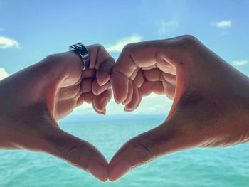 Close-up of hands against sea against sky