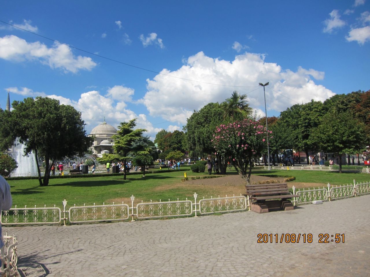 tree, sky, grass, cloud - sky, park - man made space, street light, park, cloud, green color, lawn, sunlight, incidental people, growth, footpath, shadow, nature, outdoors, empty, sport, cloudy