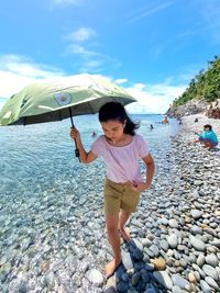 A girl wading on a rocky shore holdin an umbrella
