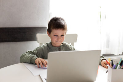 A schoolboy boy sits at a table in front of a laptop and studies dma. distance learning for children