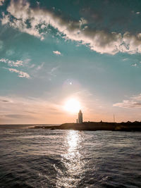 Scenic view of sea by lighthouse against sky during sunset