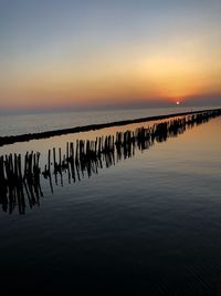Wooden posts in sea against sky during sunset