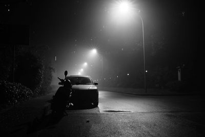 Car and motor scooter on illuminated street at night