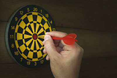 Cropped hand of person holding dart by target hanging on wall