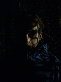 Portrait of young woman standing against black background