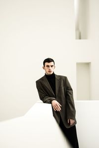 Portrait of young man sitting against wall