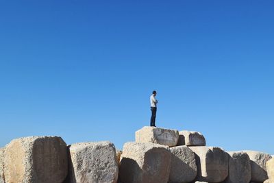 Full length of man standing on rocks against clear blue sky