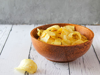 Potato chips or crisps in wooden bowl against white wooden background. pile of potato chips. 