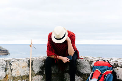 Man sitting on rock looking at sea shore against sky