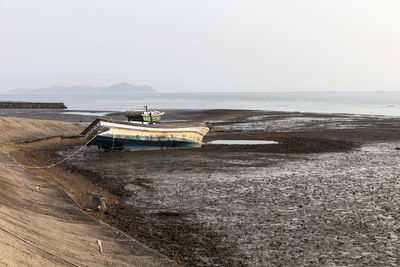 Abandoned boat moored on shore during low tide