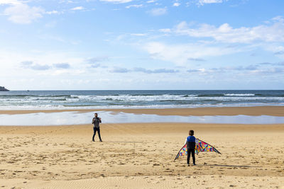 People playing with kite at beach against sky