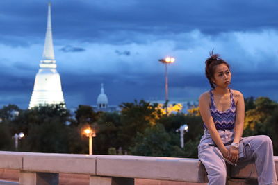 Woman sitting on tower in city against sky