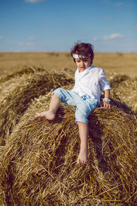 Boy child in bandana and white shirt sitting on a bale of hay in the summer